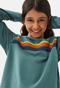 Teal langärmliges Shirt mit einem gestreiften Design in Marineblau, Orange und Gelb auf der Brust, aus weichem Baumwollmaterial mit lockerer Passform.