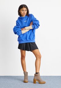 Blue oversized hoodie with logo, paired with a black pleated skirt and gray lace-up ankle boots with a thick heel and rubber sole.