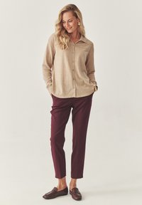 Camicia beige con colletto, abbinata a pantaloni bordeaux su misura e mocassini marroni. Tessuto liscio, vestibilità comoda e design semplice.