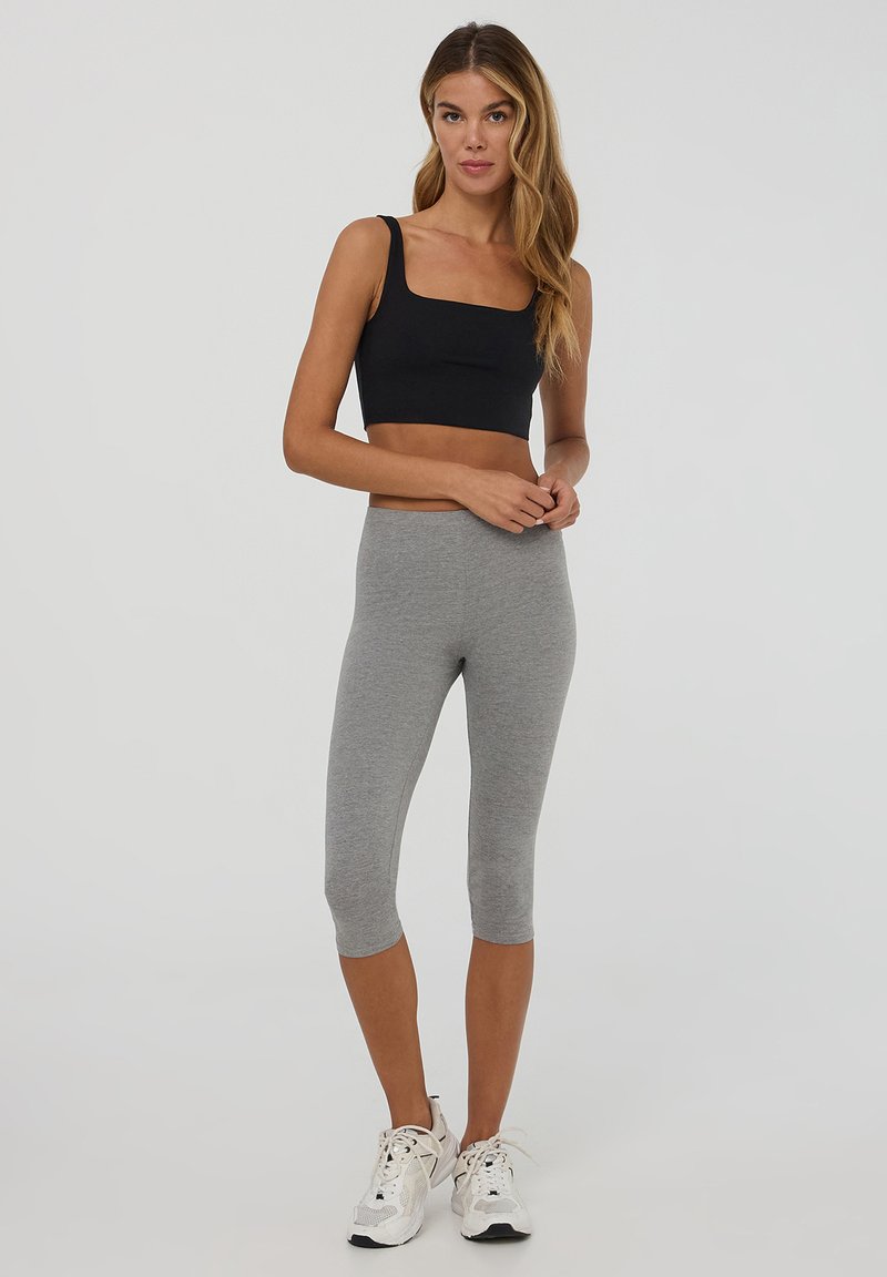 Top corto nero con scollatura quadrata e spalline sottili, abbinato a leggings grigi alla caviglia. Scarpe da ginnastica bianche completano l'outfit.