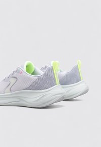 Baskets de sport gris clair avec tige en mesh, semelle arrondie et accents verts, présentant un design texturé et des languettes de traction au niveau du talon.