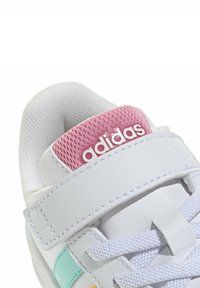 Zapatilla deportiva blanca con una lengüeta de malla rosa, acentos en azul y naranja, y una correa de Velcro. Presenta materiales texturizados y detalles con costuras.