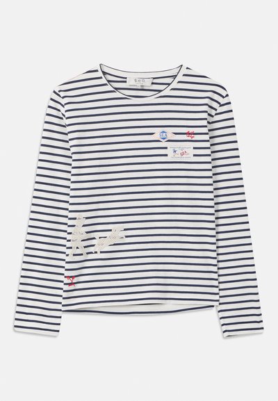 Striped long-sleeve shirt in white and navy. Features a chest pocket with patches and embroidered dogs at the hem. Soft fabric, relaxed fit.
