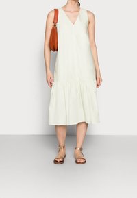 Hellgrünes, knielanges Kleid mit V-Ausschnitt, ärmellosem Design und gerafftem Rock. Abgerundet mit braunen Sandalen mit Riemchen und einer braunen Tasche.