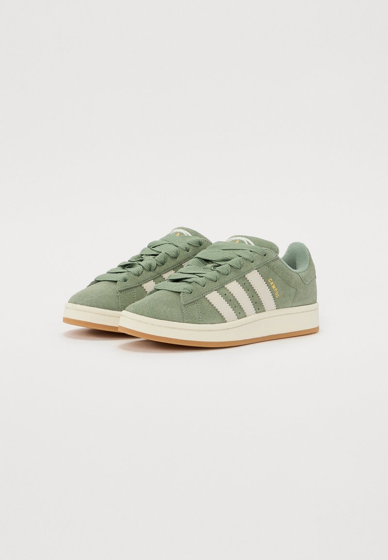 Las zapatillas de ante verde cuentan con un diseño de tres rayas blancas, puntera redonda y suela de goma beige. Cierre con cordones y detalles texturizados.