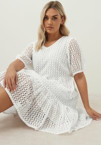 Vit klänning med puffy ärmar i strukturerad gitterväv, med V-ringning, volangfåll och knä-length siluett.