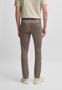 Pantalons beige ajustés en tissu lisse, dotés de poches arrière avec des rabats courbés, associés à une chemise de couleur claire et à des baskets.