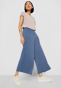 Licht beige korte mouwen top, gecombineerd met een wijde blauwe broek en crèmekleurige sneakers, met een elastische tailleband en een zachte stoftextuur.