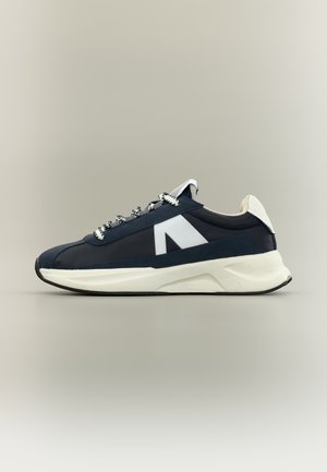 Marineblauer und weißer Sneaker mit dicker Sohle, gemusterten Schnürsenkeln und großem weißem, eckigem Logo an der Seite, im Profil gezeigt.