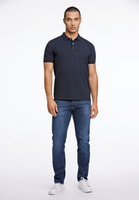 T-paita tummansinisestä kankaasta, jossa on lyhyet hihat, tasainen kaulus ja kolme nappia, yhdistettynä sinisiin farkkuihin ja valkoisiin tennareihin. Minimalistinen muotoilu.