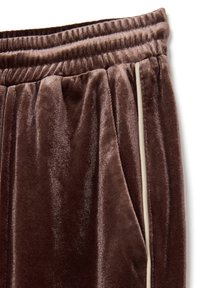 Pantalones de chándal de terciopelo marrón con una cintura elástica, con una franja de color crema a lo largo del costado y bolsillos laterales. Textura suave.