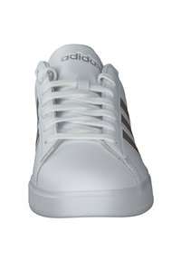 Witte sportieve schoen met een gestructureerde synthetische bovenkant, ronde neus, witte veters en drie bruine strepen aan de zijkanten. Plat rubberen zool.