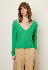 Groene, zachte, textuur cardigan met een diepe V-hals en knoopsluiting. Lange mouwen en een getailleerde taille, gecombineerd met lichtbeige broeken.