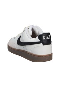 Zapatilla blanca de cuero con swoosh negro y lengüeta trasera, suela de goma marrón, puntera reforzada y lengüeta de malla para ventilación.