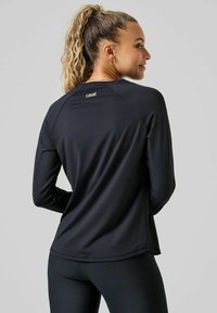 Zwart sportshirt met lange mouwen, een gladde textuur, raglanmouwen, een subtiel logo op de rug en een ronde zoom, gecombineerd met zwarte leggings.