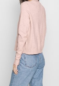 Suéter de punto color rosa claro con dobladillo y puños acanalados, diseño recortado, usado sobre jeans azul de cintura alta. La textura parece suave.