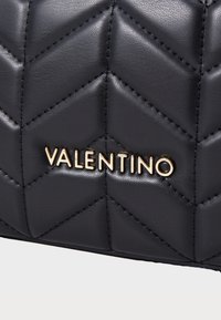 Černá prošívaná kožená kabelka s motivem šikmého vzoru a zlatým logem "Valentino" v moderním písmu. Hladký povrch s detailním prošíváním.