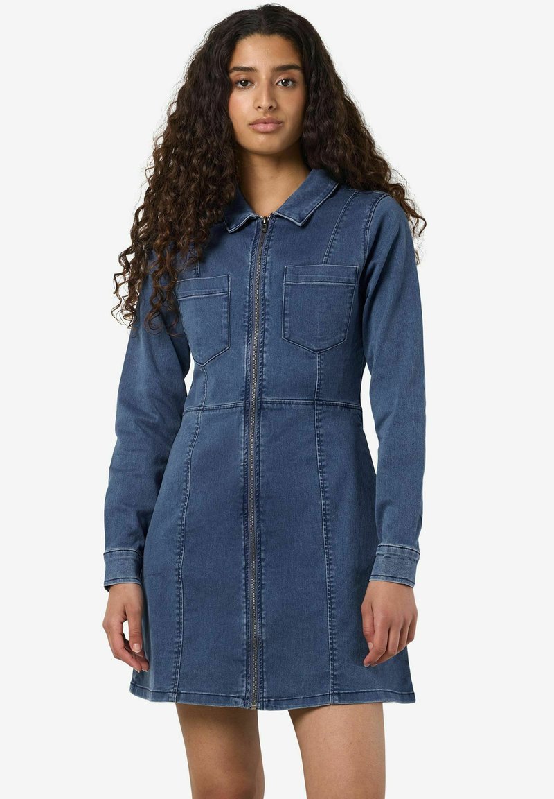Denimkjole i mørkeblå, med glidelås, spiss krage og to brystlommer. Myk tekstur med elegant, tettsittende design.