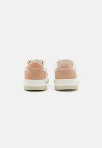 Sneakers bianche con dettagli in camoscio pesco, caratterizzate da una suola in gomma testurizzata e branding impresso sul tallone. Design minimalista.