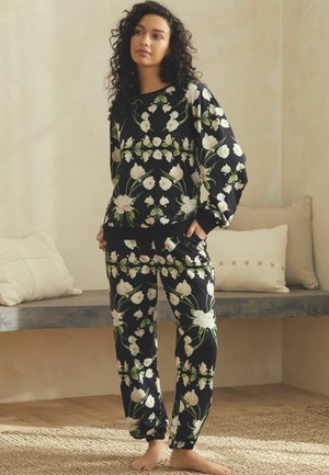 Floral loungewear set featuring black fabric with white and green floral print, relaxed fit, long sleeves, and elastic cuffs on pants.