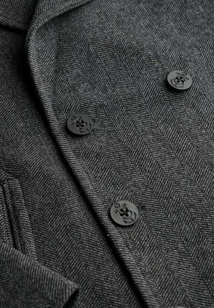 Grå herringbone blazer med sorte knapper med ankerdesign, der viser et tekstureret, skræddersyet stof og en klassisk krave.