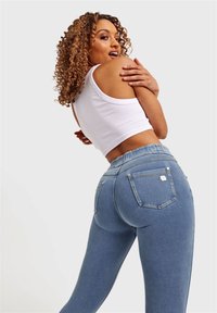 Vaqueros de mezclilla azul claro de talle alto con tela texturizada, bolsillos traseros y detalles de herrajes en tono plateado. Modelo con un top corto blanco.