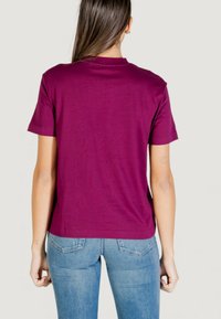 Camiseta de manga corta color granate hecha de algodón suave. Cuenta con cuello redondo y un ajuste cómodo. Combinada con jeans de mezclilla azul.