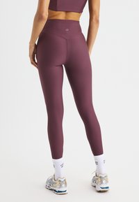 Vinröda ribbade leggings med hög midja, med en sömlös design. Bärs med vita strumpor och löparskor. Bakifrån.