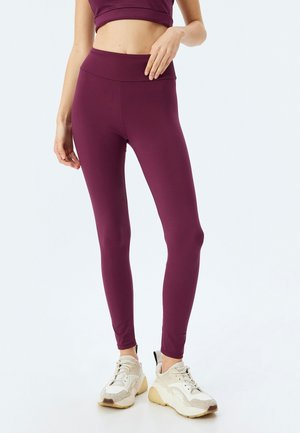 Maroon leggings med hög midja och elastiskt material. Tillsammans med vita sportskor med beige detaljer. Slät textur.