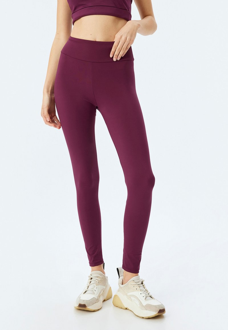 Maronfarvede leggings med høj talje og strækbart stof. Sammen med hvide atletiske sko med beige detaljer. Glat tekstur.