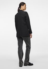 Černý tailored blazer se strukturovaným designem, s jedním rozventilovaným zadním dílem, kombinovaný se šedými džíny a černými robustními botami.