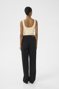 Top a canotta color crema con spalline borchiate, abbinato a jeans neri a vita alta e dalla vestibilità ampia. Tessuto liscio e design a gamba dritta.
