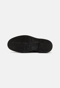 Suela de zapato negra con un patrón texturizado, que presenta un diseño de suela geométrica para ofrecer agarre y durabilidad. Fabricada en material de goma.