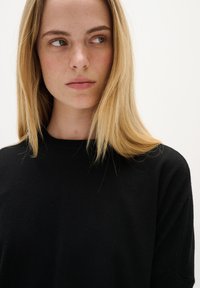 Schwarzer Strickpullover mit Rundhalsausschnitt und langen Ärmeln. Das Model hat glattes, blondes Haar und einen neutralen Gesichtsausdruck.