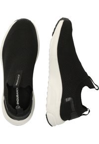 Mustat neulotut slip-on urheilukengät valkoisilla kumipohjilla ja teksturoidulla yläosalla, joissa on vetonauha ja musta yksityiskohta kantapäässä.