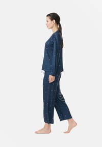 Mörkblå pyjamasset med långärmad topp och byxor som har små ljusblå stjärnmönster, tillverkad av mjukt tyg, avslappnad passform.