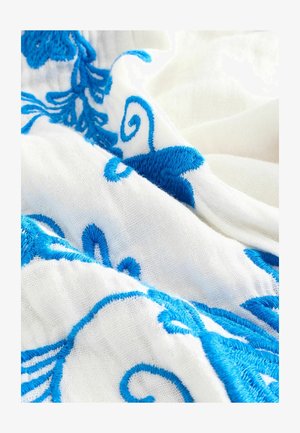 Witte stof met ingewikkelde blauwe borduursels toont bloem- en spiraalpatronen, met een zachte textuur en gedetailleerde ambacht.