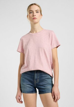 T-shirt rosa a maniche corte con scollatura rotonda e un aspetto testurizzato, abbinato a pantaloni corti di jeans a vita alta.