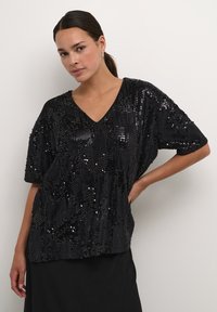 Black sequined top with short sleeves and a V-neck. Features a loose, relaxed fit and a textured surface created by the sequins.