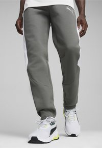 Szare dresy Puma z białymi panelami bocznymi, charakteryzujące się gładką teksturą i zwężanym krojem. W połączeniu z białymi i zielonymi butami do biegania.