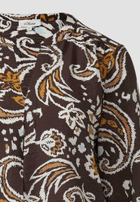 Bruine blouse met een paisleypatroon in wit, roest en lichtblauw. De stof heeft een gestructureerde uitstraling met zachte, geraffineerde details bij de halslijn.