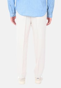 Camicia di denim azzurro chiaro con orlo curvo e polsini con bottoni, indossata con pantaloni plissettati color crema e sneaker in camoscio grigio.