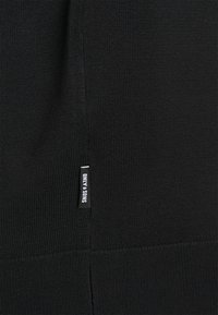 Pull noir en maille avec un motif texturé, poignets et ourlet côtelés, avec une petite étiquette de marque cousue sur le côté.