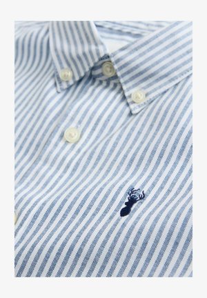 Lyseblå og hvid stribet skjorte med knapper og spidst krave. Har en lille broderet hummel-logo på brystet. Tekstureret stof.