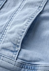 Close-up of light blue denim fabric showing detailed stitching and texture of a pocket area.