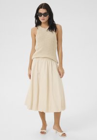 Beige stickad tanktopp matchad med en flödande, ljusbeige midikjol. Skorna har en låg klack i en matchande färg.