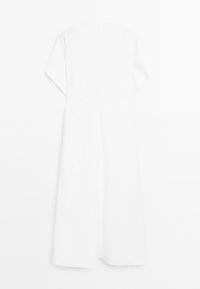 Un vestito bianco semplice, lungo fino al ginocchio, pende su uno sfondo neutro, con maniche corte e larghe e una chiusura con zip sul retro.