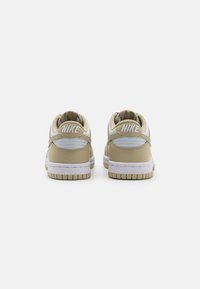 Baskets Nike beiges avec accents blancs, col rembourré et cuir texturé. Possède un logo sur le talon, une semelle en caoutchouc et un bout rond.