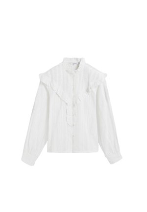 Blusa blanca con cuello volado, botón al frente y mangas largas. La tela texturizada presenta sutiles líneas verticales.