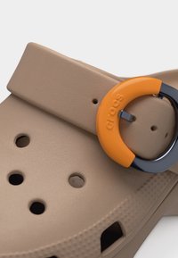 Μπεζ σανδάλι Crocs με στρογγυλή πορτοκαλί και μαύρη αγκράφα στο λουράκι, με οπές αερισμού στην επάνω επιφάνεια.